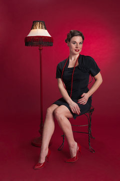 Pinup Girl in Black Dress Sits with Fringed Lamp