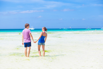 back view of couple holding hands in water on tropical beach in