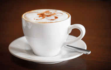 One white cup of cappuccino stands on dark wooden table