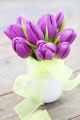 Bouquet of purple tulips in vase on wooden background