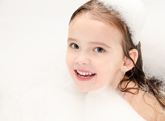 Smiling little girl washing in bath with foam