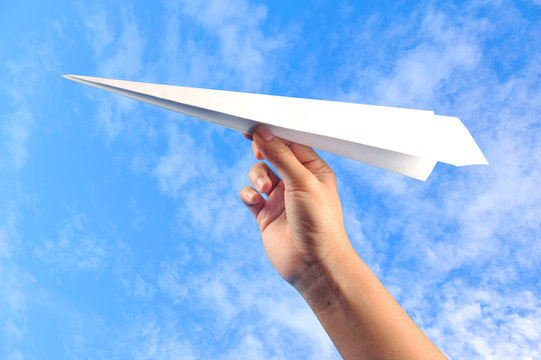 hand with paper plane against blue sky