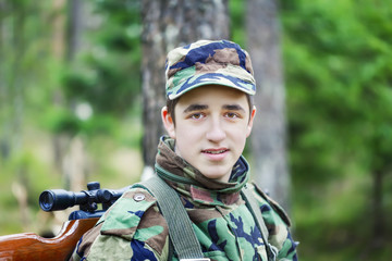 Young recruit with optical rifle in the woods