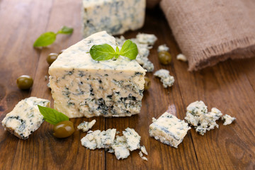 Obraz na płótnie Canvas Tasty blue cheese with olives and basil, on wooden table