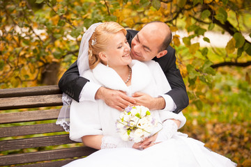 middle aged groom kissing bride sitting on bench