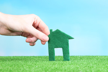Little paper house in hand on green grass on bright background