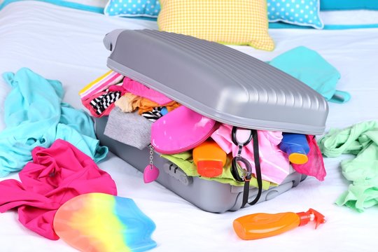 Grey suitcase with clothing on bed close-up