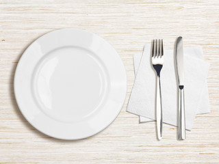 white plate, knife, fork and napkin top view on wooden table