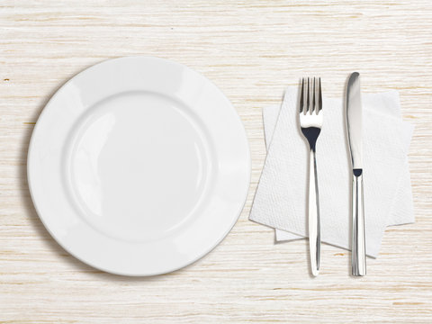 White Plate, Knife, Fork And Napkin Top View On Wooden Table