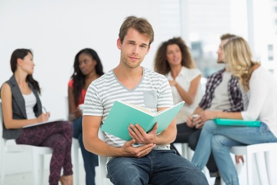 Happy man holding notebook while colleagues are talking behind