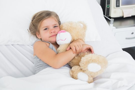 Cute girl embracing teddy bear in hospital bed