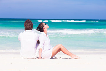 happy young couple in white clothes in sunglasses lying on beach