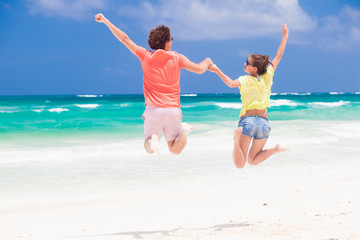 Young couple in bright clothes jumping on the beach looking on