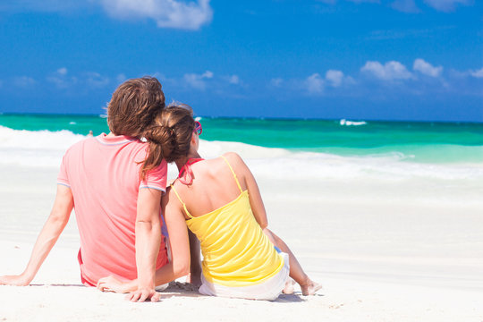 Young couple in bright clothes sitting on the beach looking on