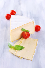 Tasty Camembert cheese with tomato and basil, on wooden table