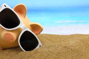 Summer piggy bank with sunglasses on the beach