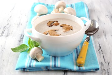 Mushroom soup in white pot, on napkin,  on wooden background