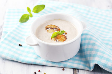 Mushroom soup in white pot, on napkin,  on wooden background