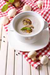 Mushroom soup in white pot, on napkin, on wooden background