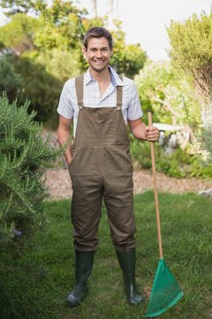 Young man in dungarees holding rake in garden