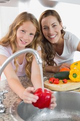 Portrait of young girl helping her mother to wash vegetables