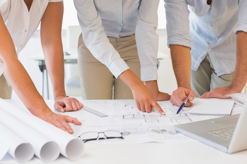 Mid section of business people working on blueprints at office