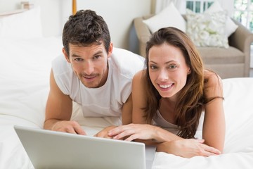 Fototapeta premium Smiling couple using laptop in bed