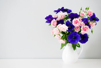 Bouquet of pink roses and blue anemones in white vase on grey ba