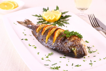 Grilled sea bream fish, lemon, arugula on white plate
