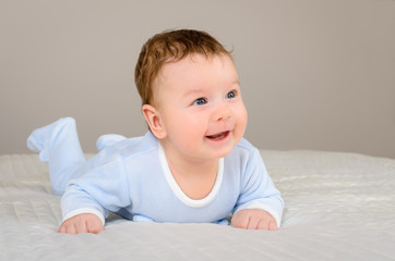 Fototapeta premium Cute smiling baby boy in bed lying on his belly in bedroom
