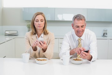 Business couple text messaging while having breakfast in kitchen