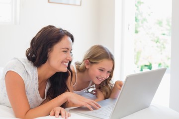 Woman with daughter using laptop in bed