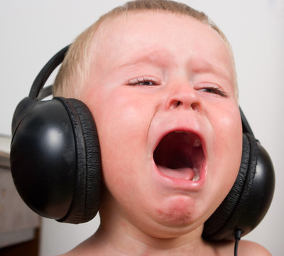 Little boy listening in stereo headphones crying and screaming