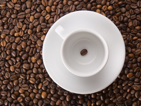 A white cup with one coffee bean on beans background © vladis_studio