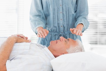 Obraz na płótnie Canvas Therapist performing Reiki over senior man