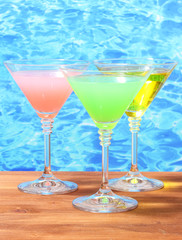 Glasses of cocktails on wooden table on blue sea background