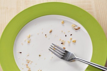 Plate with crumbs and used fork on wooden background
