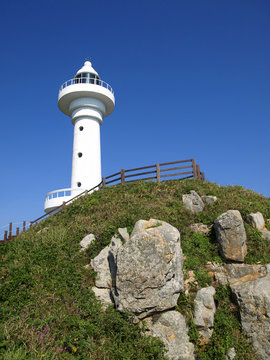 white lighthouse on top of green rocky hill