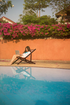 Young woman working with laptop near the pool in the tropics