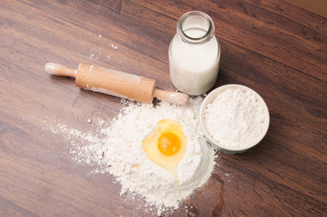Fototapeta na wymiar Egg in a flour hill and a bottle of milk
