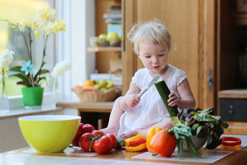 Toddler girl cutting cucumber preparing healthy vegetables salad