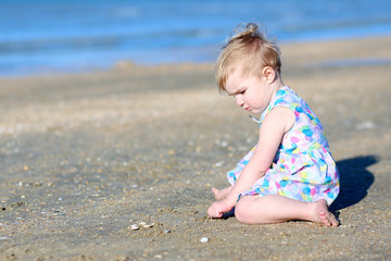 Girl plays with seashells sitting at s shore of the sea