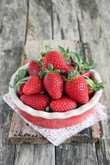 Fresh strawberries in the red ceramic dish on wooden background.
