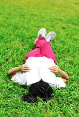 woman college student lying down on grass with book in hands