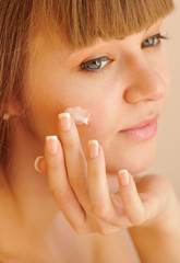Beauty face of young woman with cosmetic cream on a cheek
