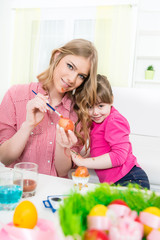 Fototapeta premium Happy sisters coloring Easter eggs and looking at camera