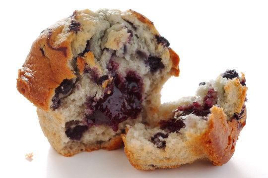 Broken blueberry muffin on white surface