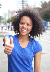 Young woman with curly hair in the city showing thumb up