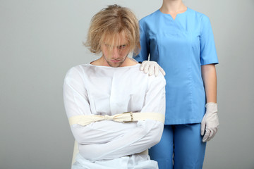 Mentally ill man in strait-jacket on gray background