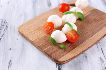 Tasty mozzarella cheese with basil and tomatoes, on wooden